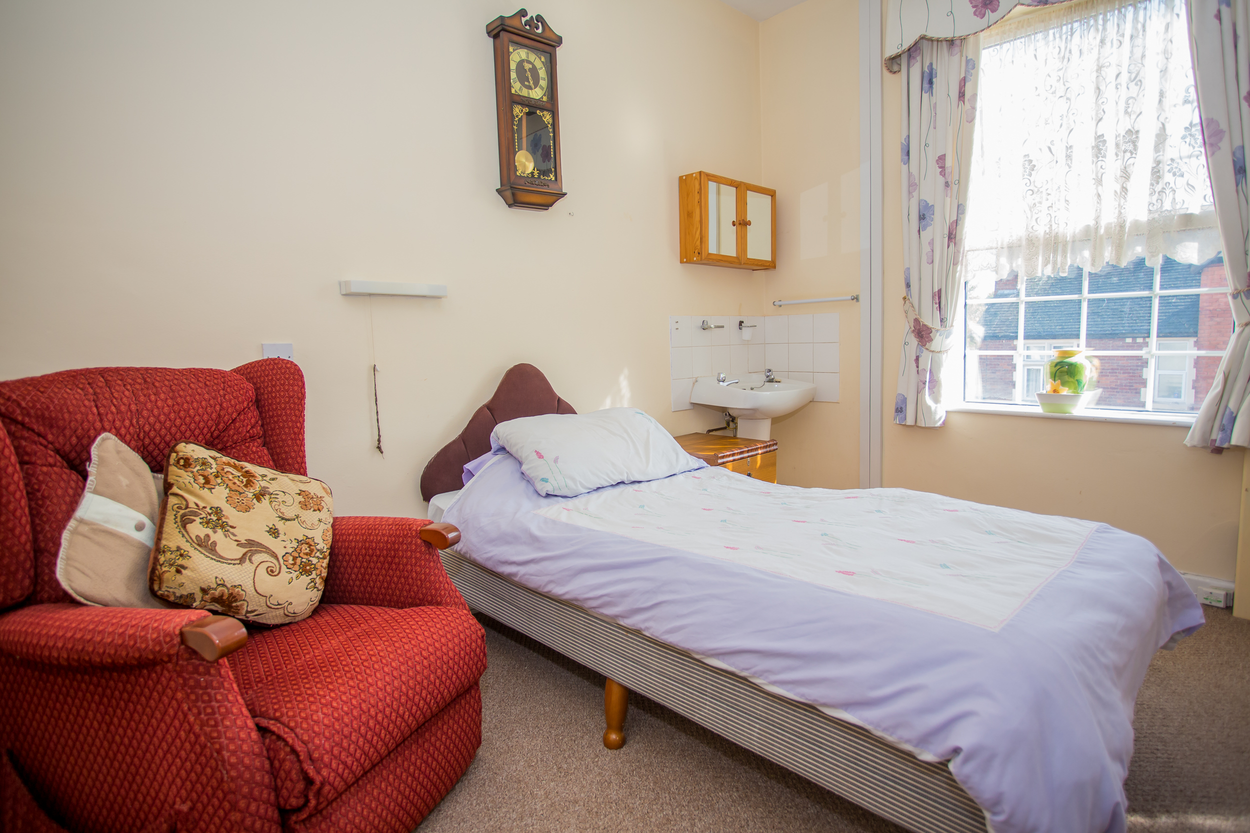 A bedroom with a red armchair, a bed, and a window